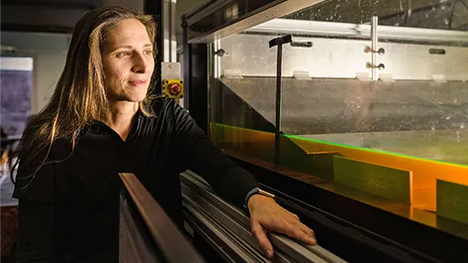 A woman stands in a darkened laboratory next to a shallow tank of water that glows green.