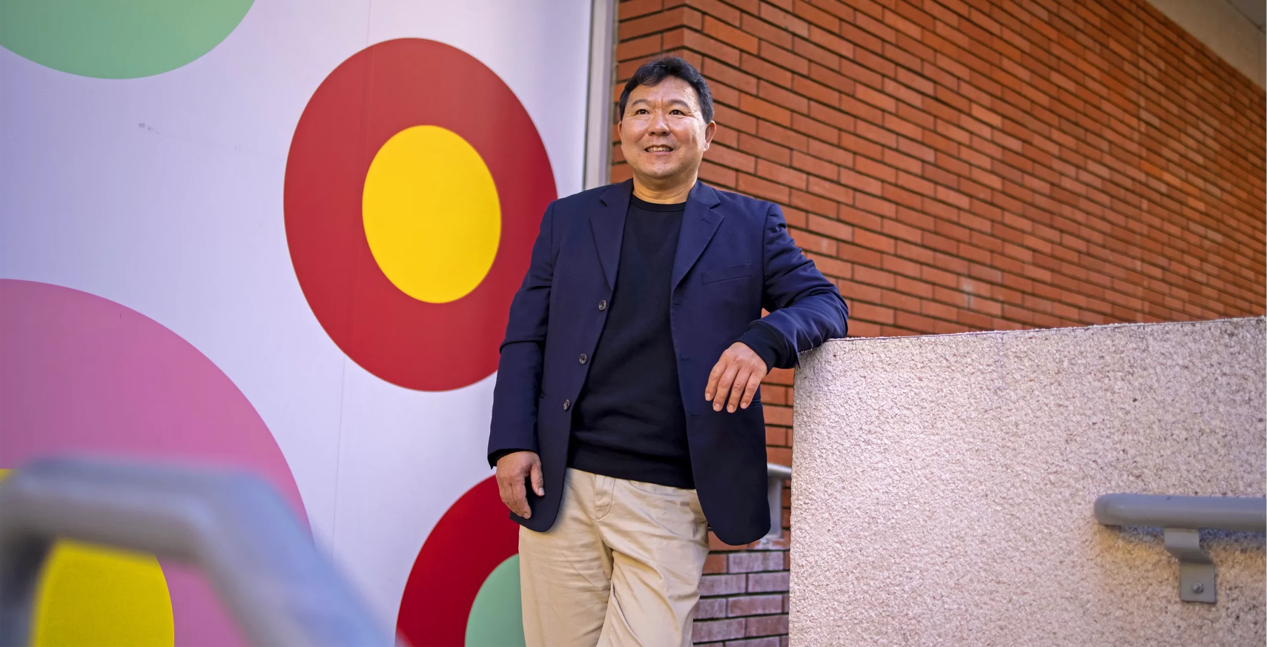 Teng leans against a staircase in front of a brick wall and a painting of circles