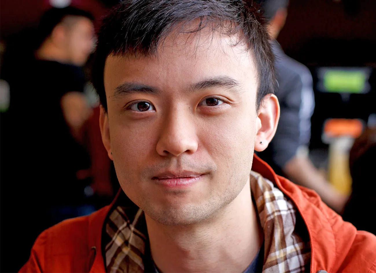 A close up of a young man with dark hair and dark eyes looking into the camera with a slight smile