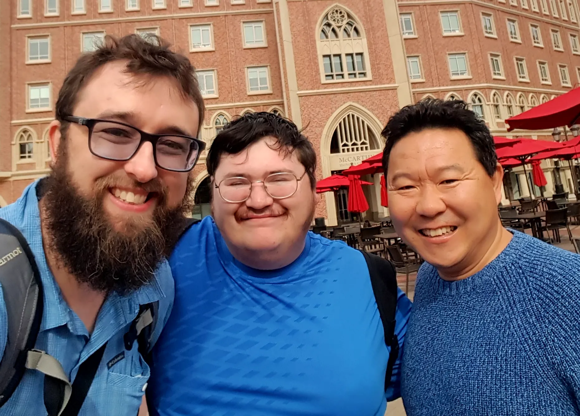 Kyle Burke, Matthew Ferland and Teng outdoors in front of tables and a brick building