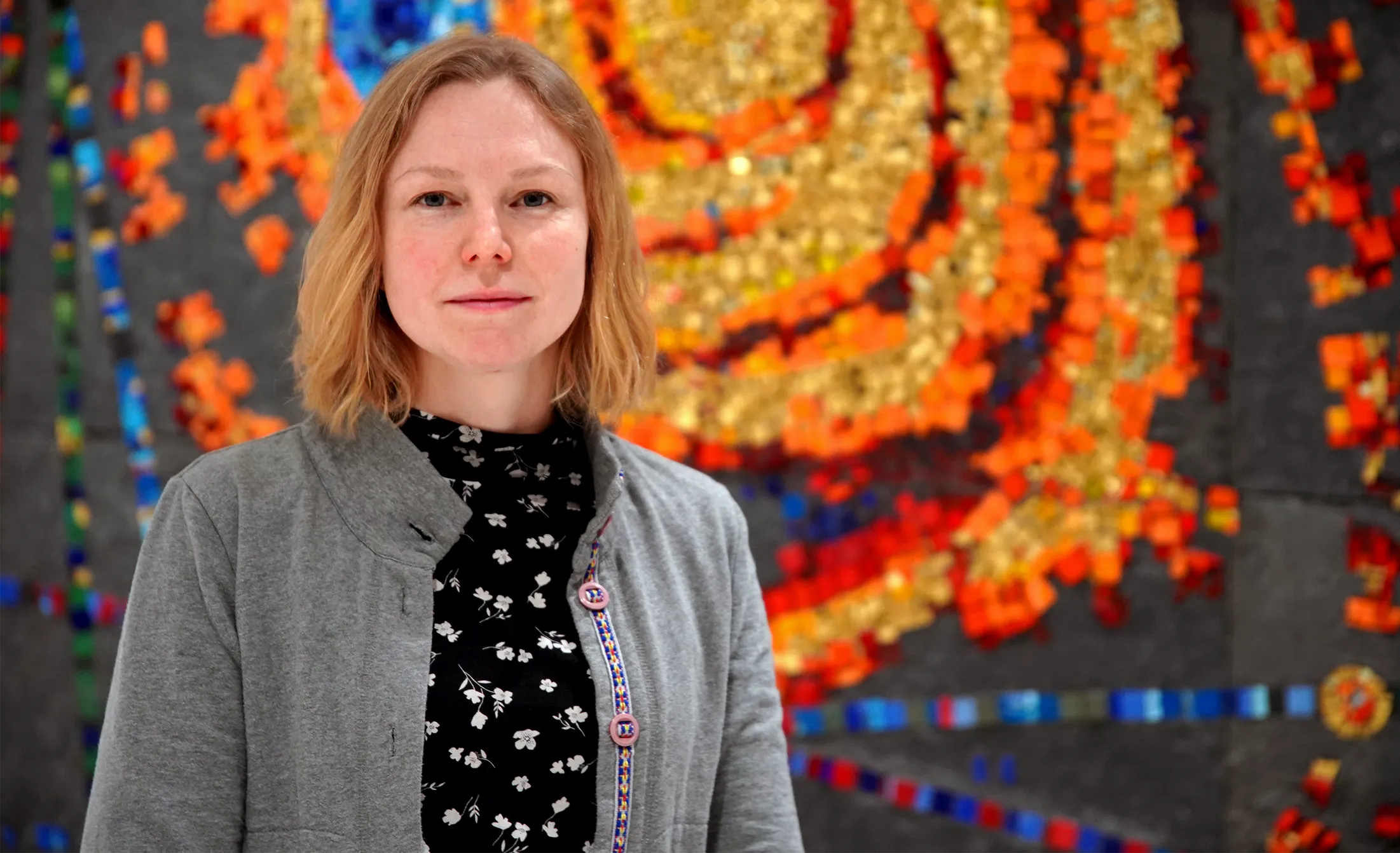 A blonde woman poses in front of a wall hanging displaying astronomical objects.