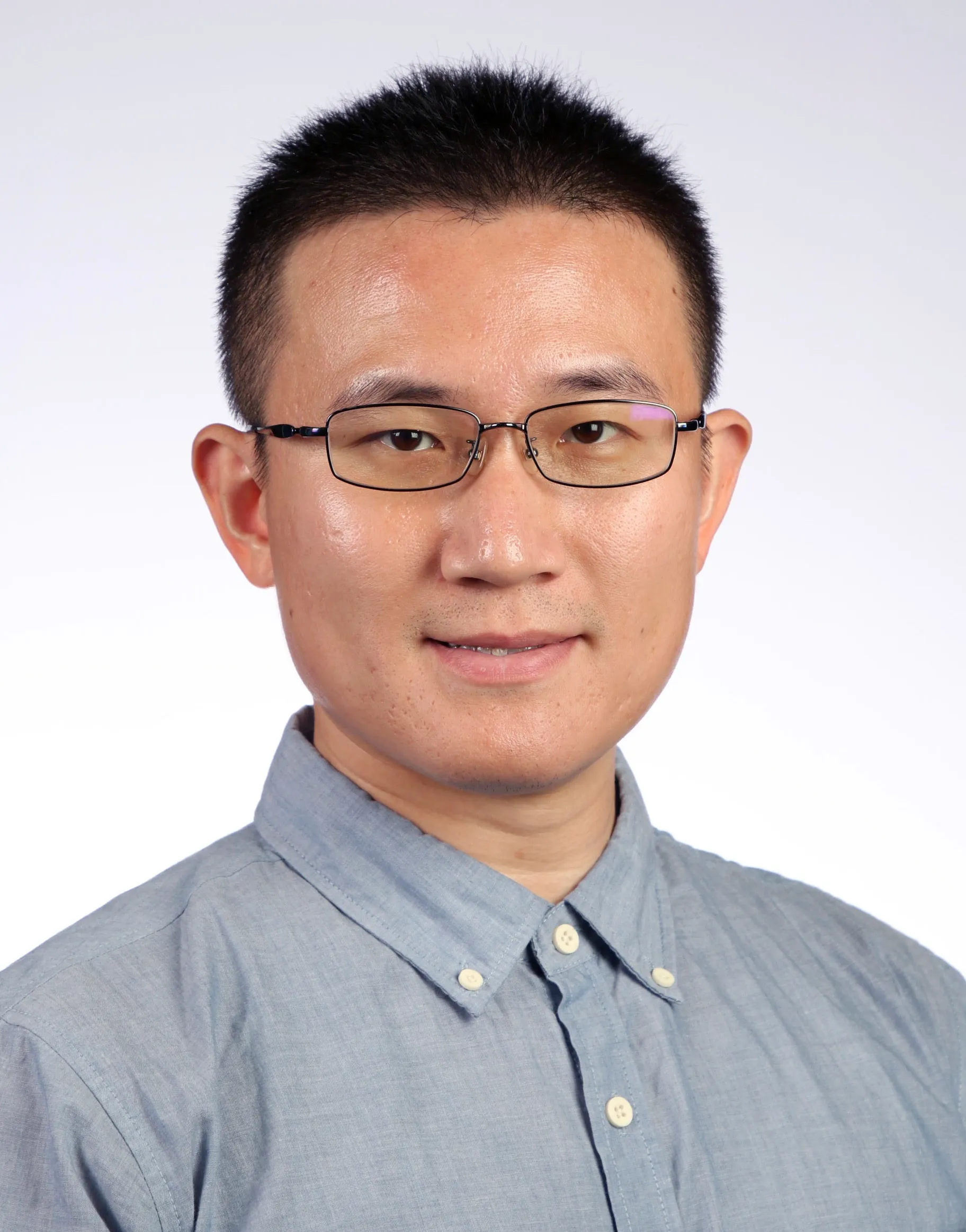 Portrait of a young man with short hair and glasses wearing an Oxford shirt.