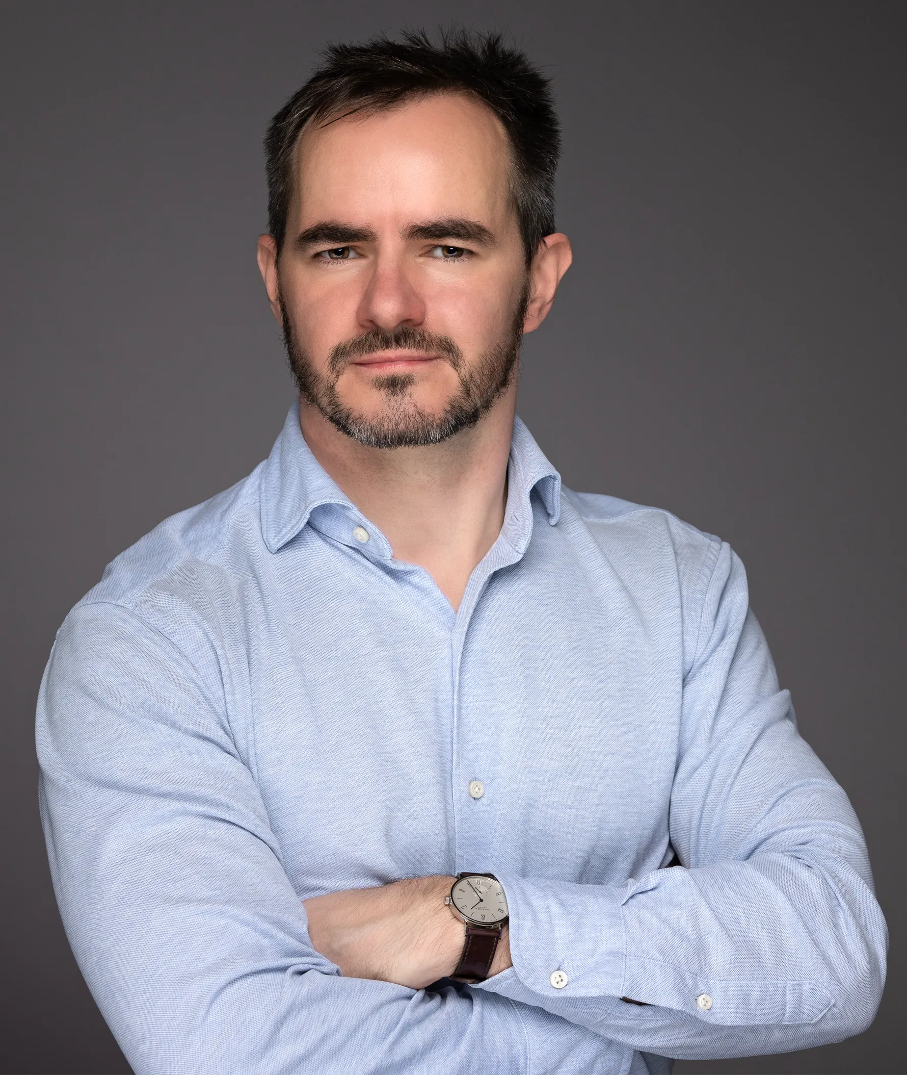 Danilo Bzdok with his arms crossed in front of a dark background.