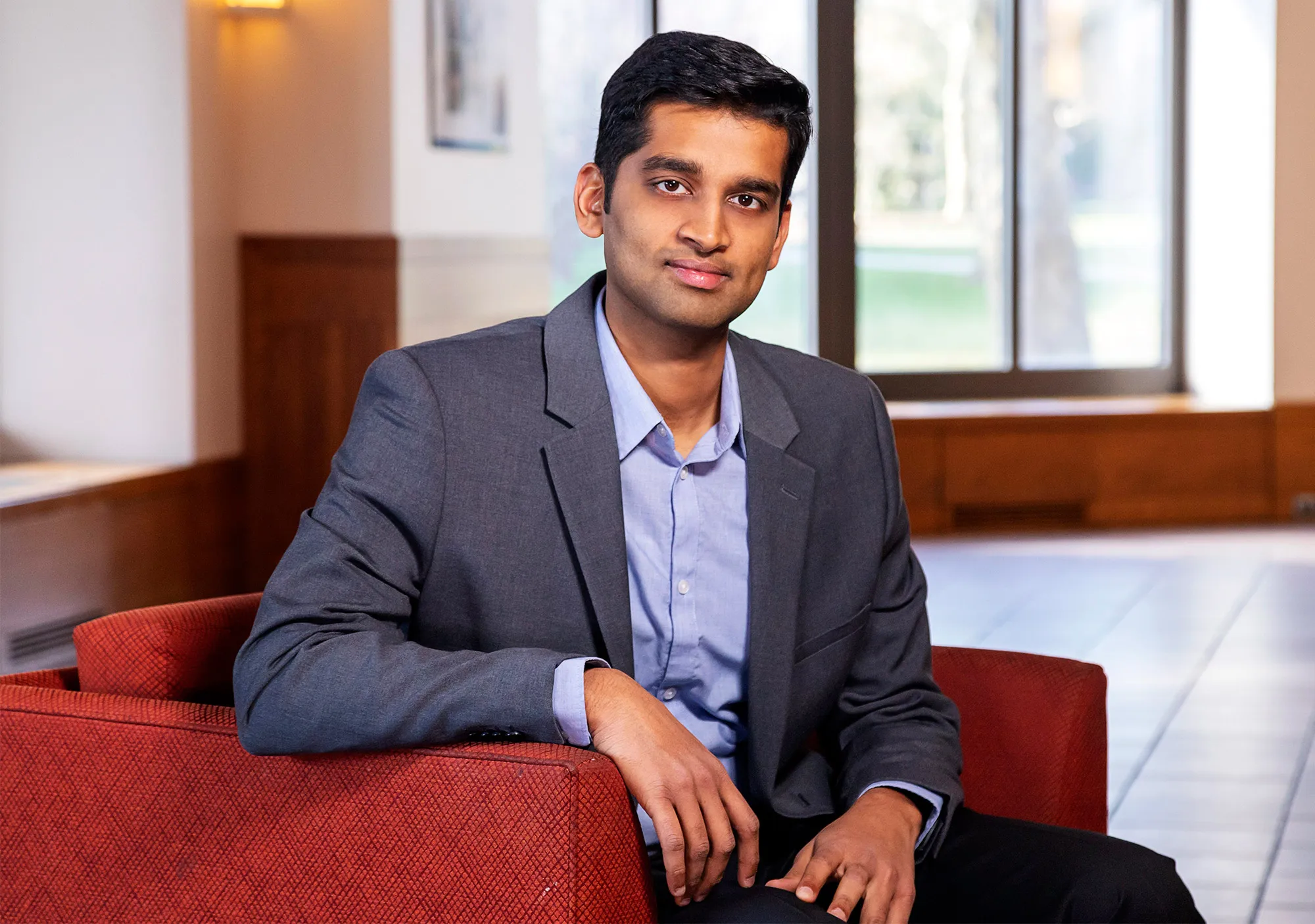 Karthik Narasimhan in a blue shirt and gray blazer sits in a red chair