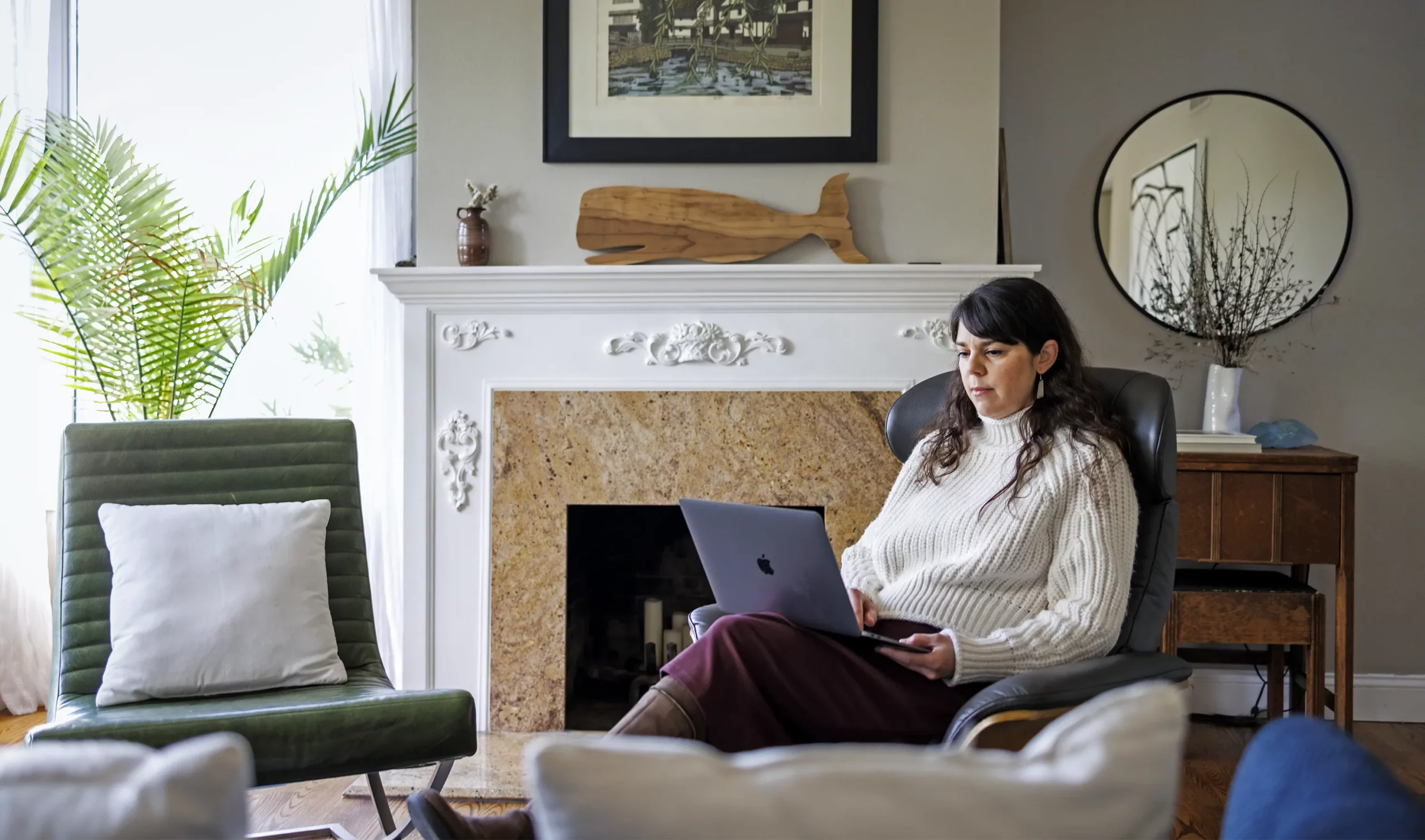 Kristy Red Horse seated with a laptop beside a fireplace in her living room.