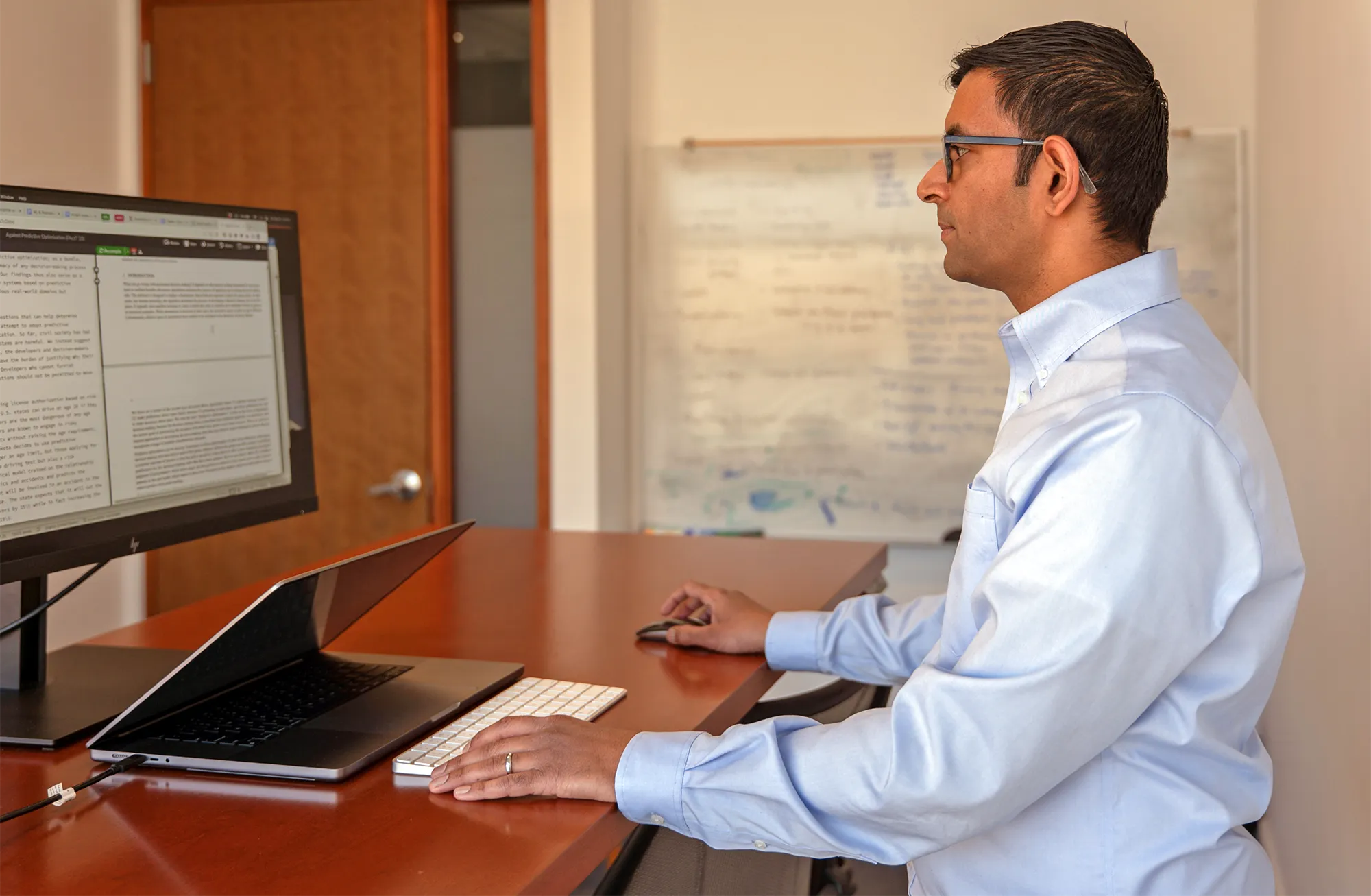 Narayanan sits at a brown desk looking at a monitor