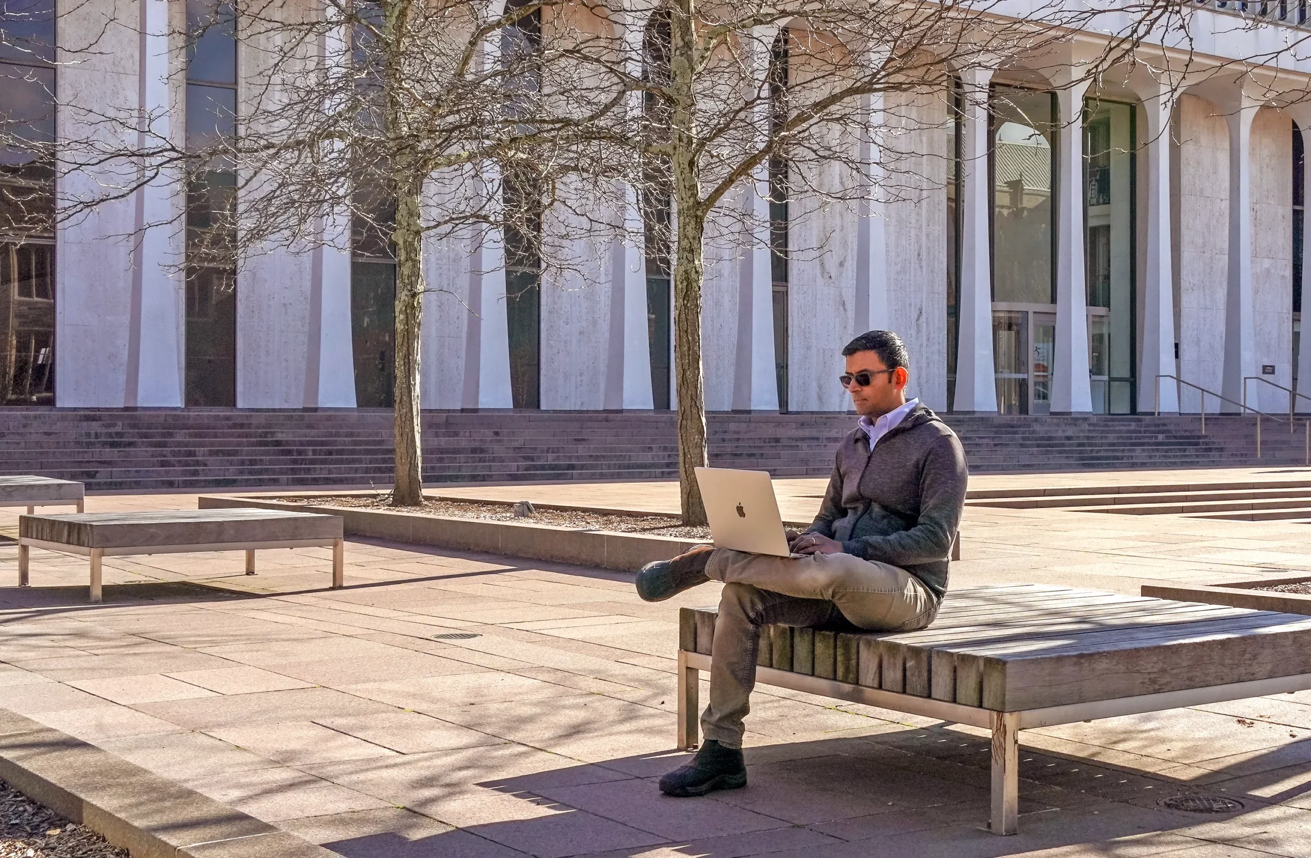 Naryanan sits on a bench outdoors working on a laptop