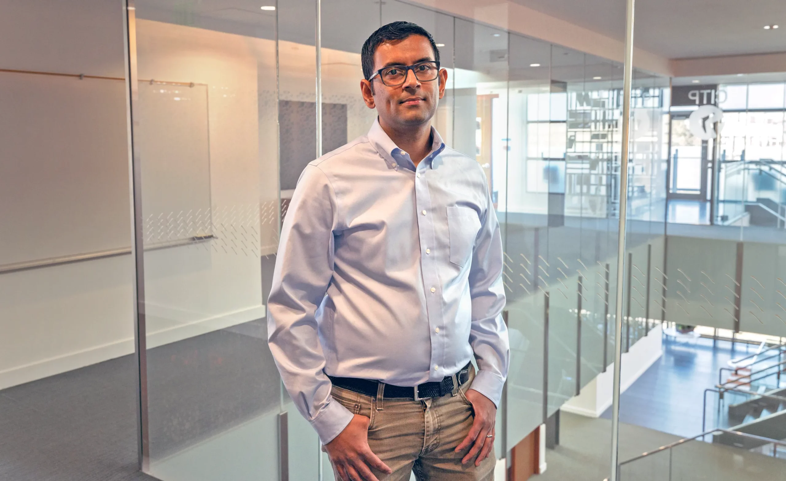 Narayanan stands in front of a glass wall inside an office building