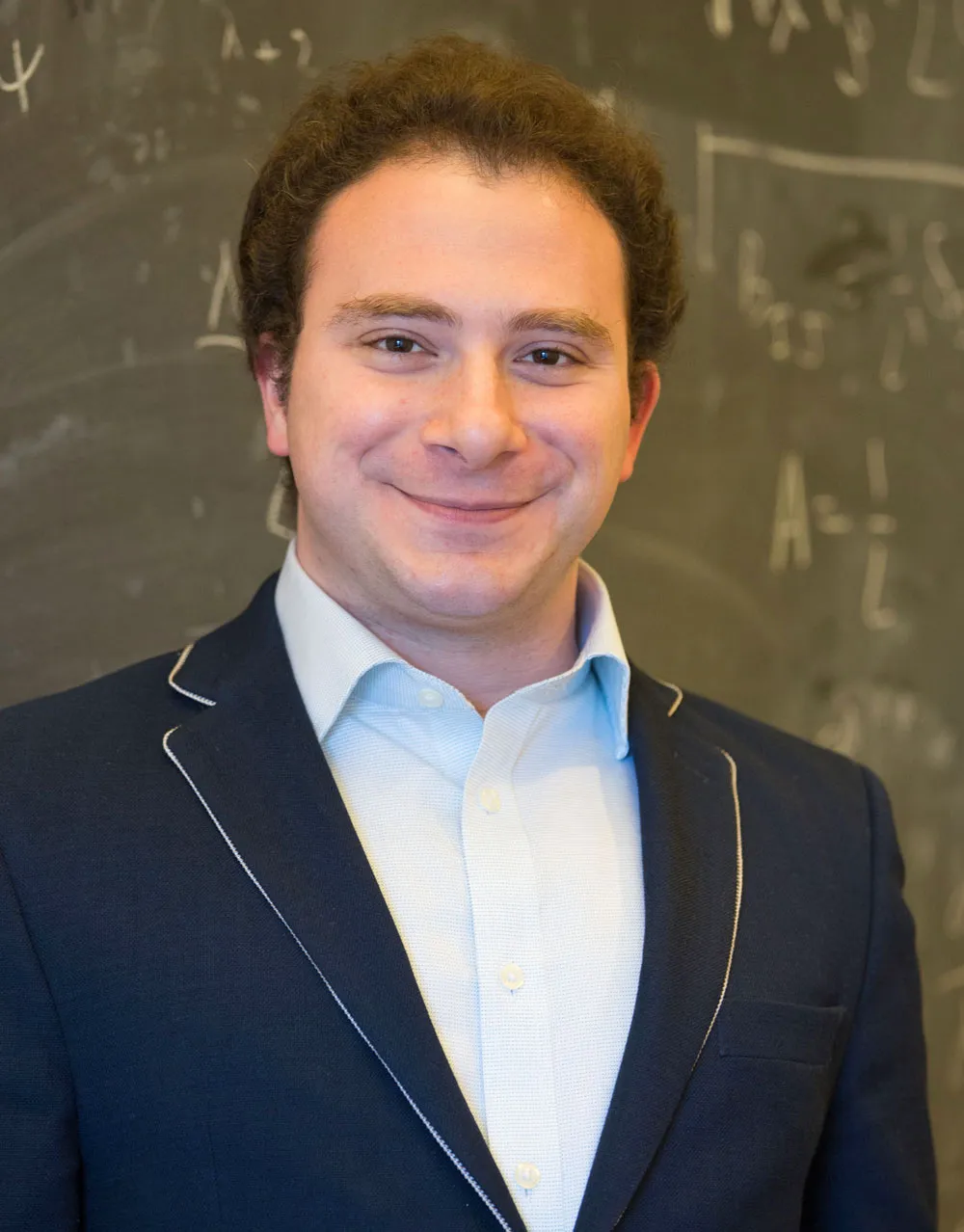 A smiling man in front of a chalk board.