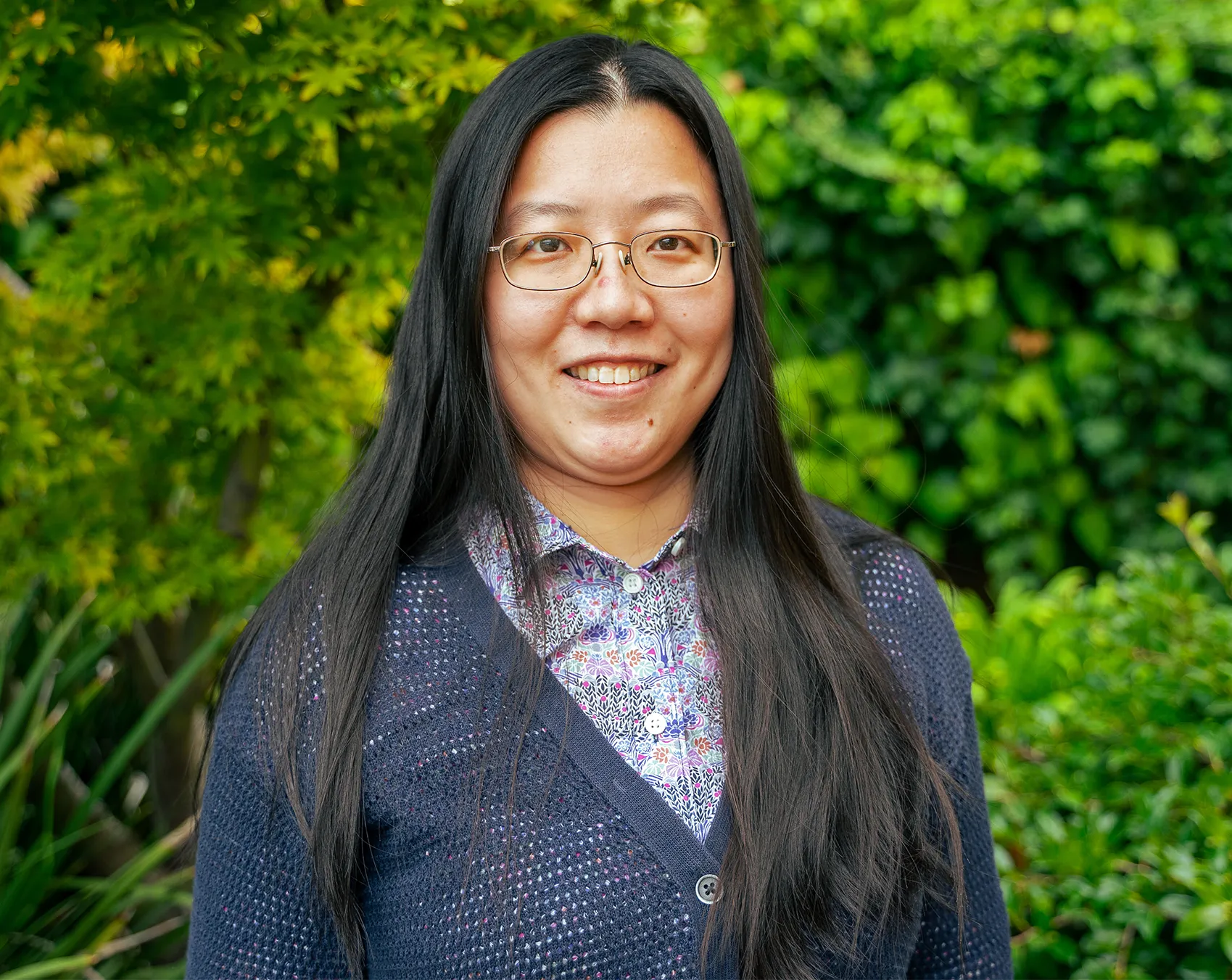 A portrait of Yunqing Tang standing in front of green bushes.