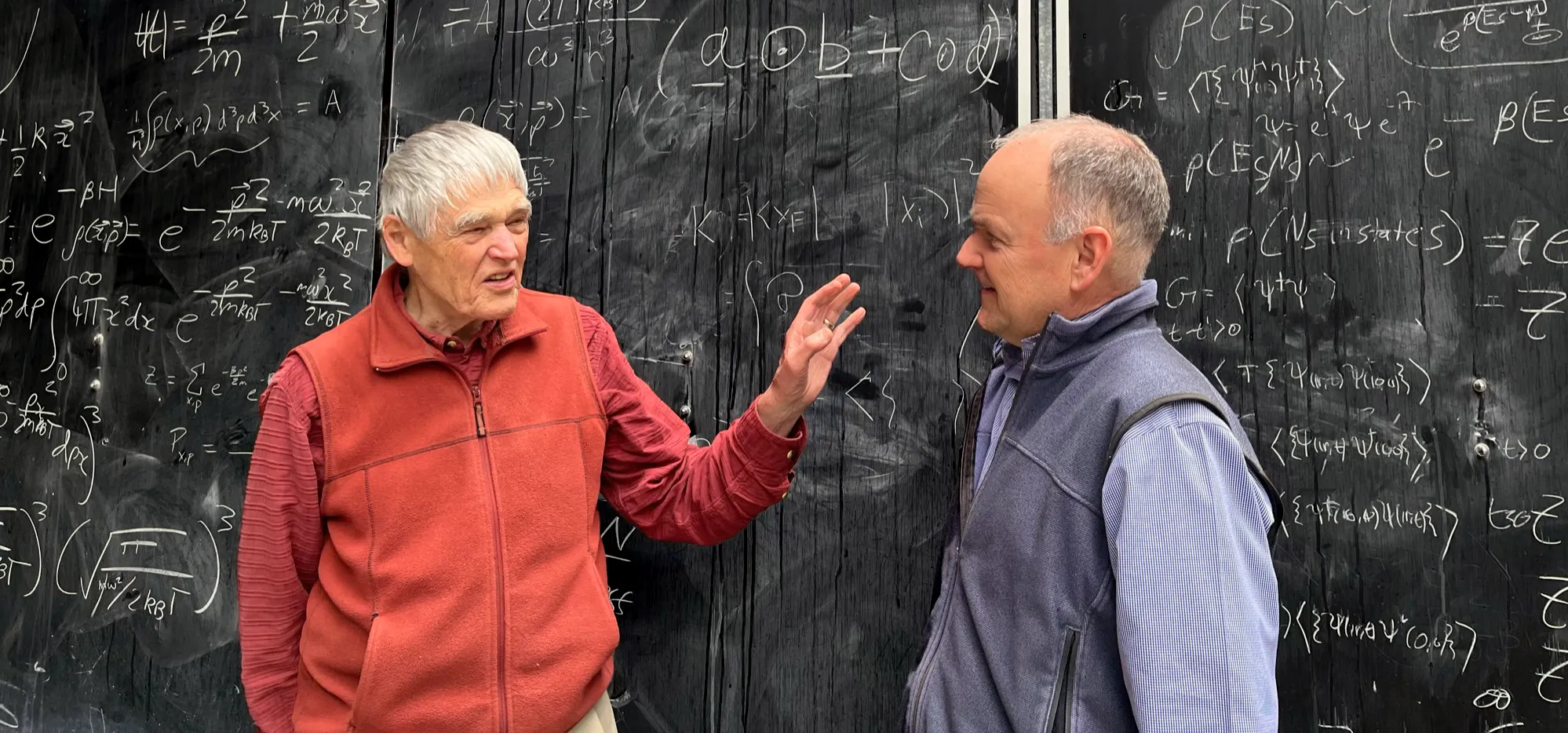 Two men in front of a chalk board.