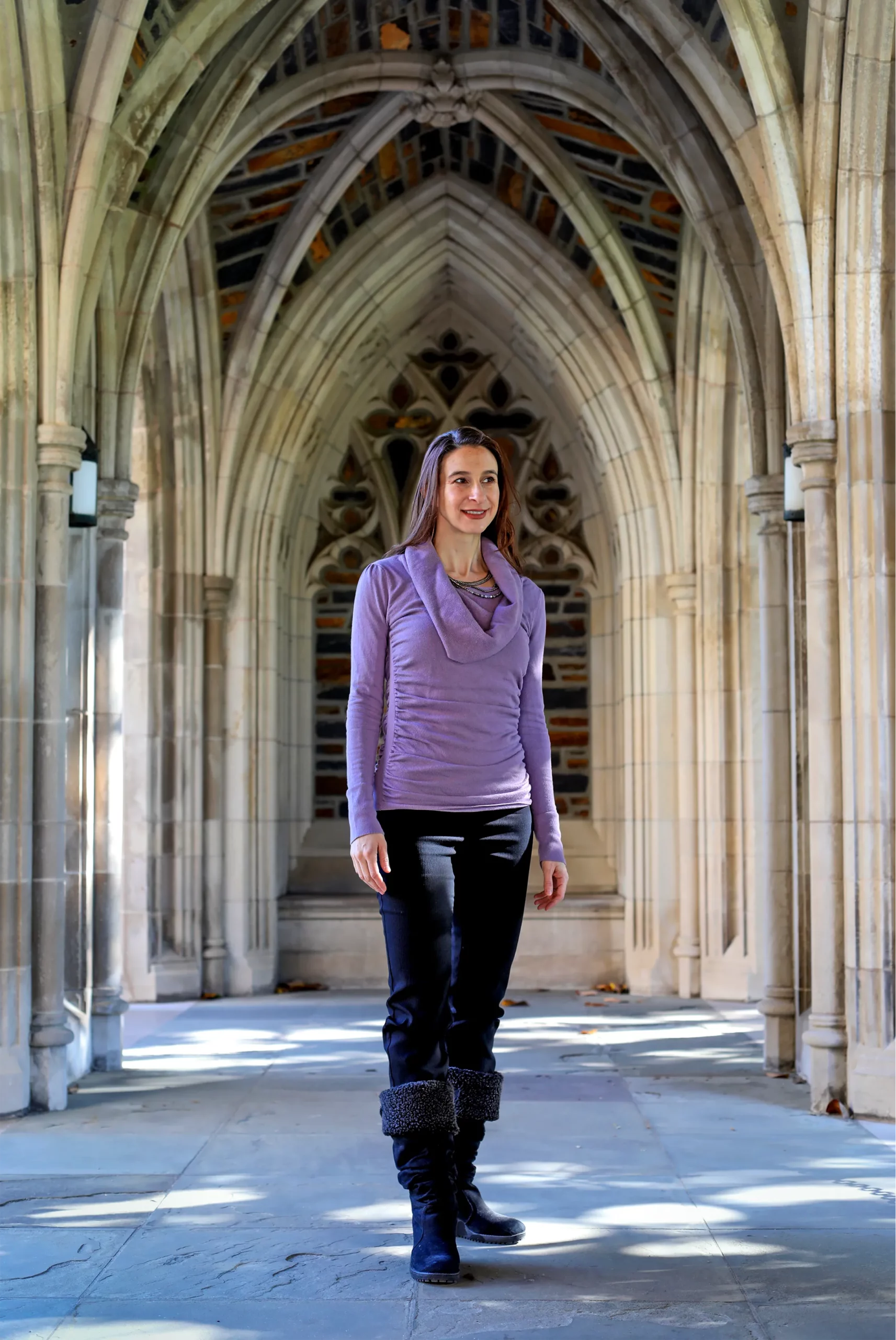 Cynthia Rudin, in a purple sweater and black pants, stands under stone arches.