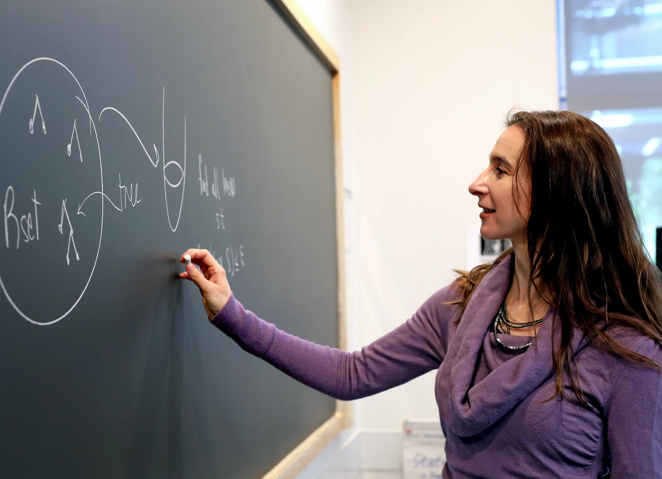 Cynthia Rudin, in a purple sweater, writes on a chalkboard.