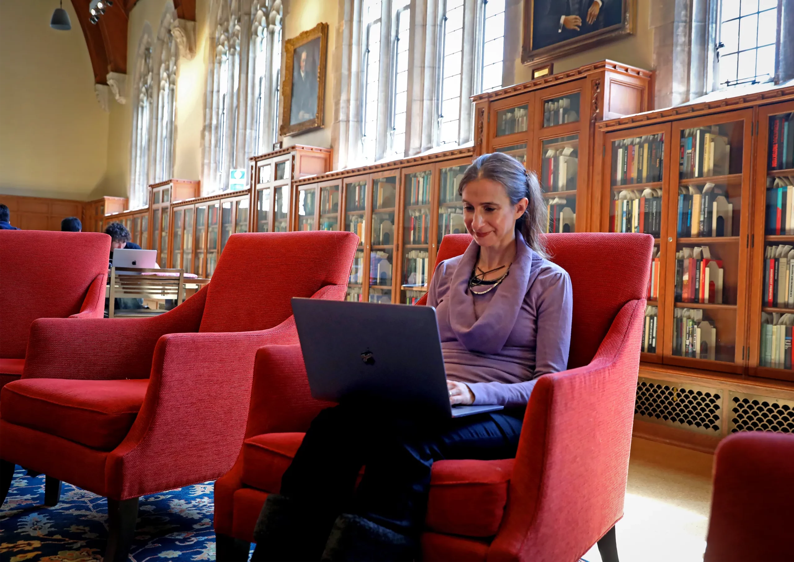 Cynthia Rudin sits with a laptop in a red chair in front of several bookshelves.