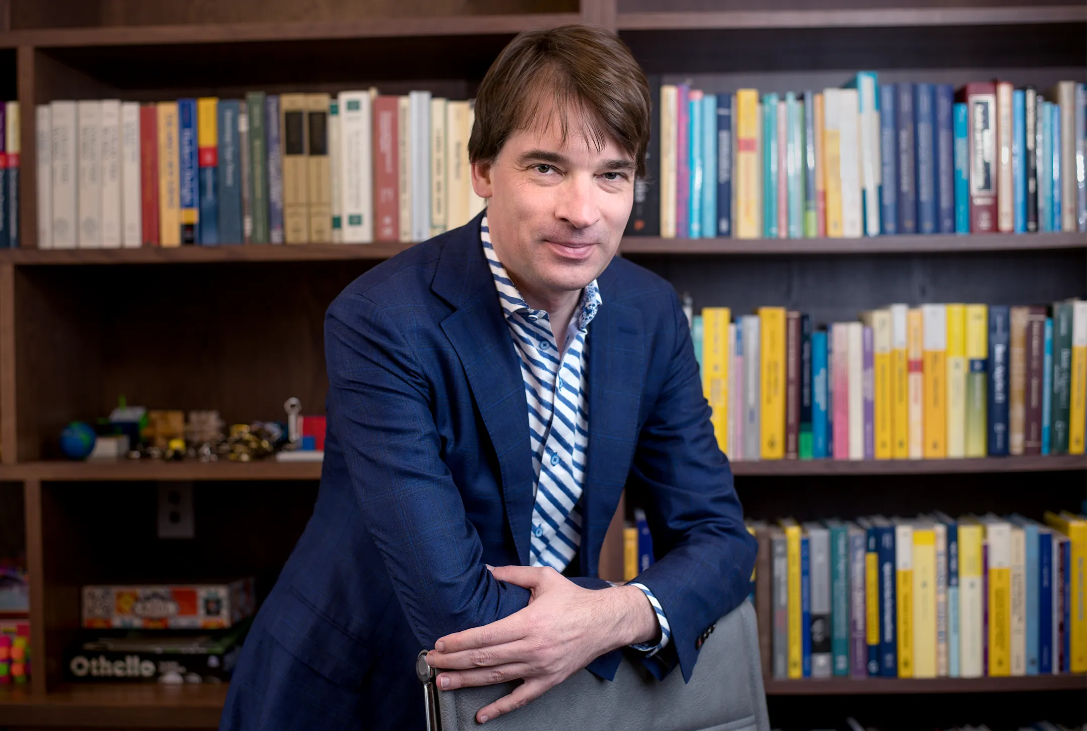 A man leaning on a chair in a library.