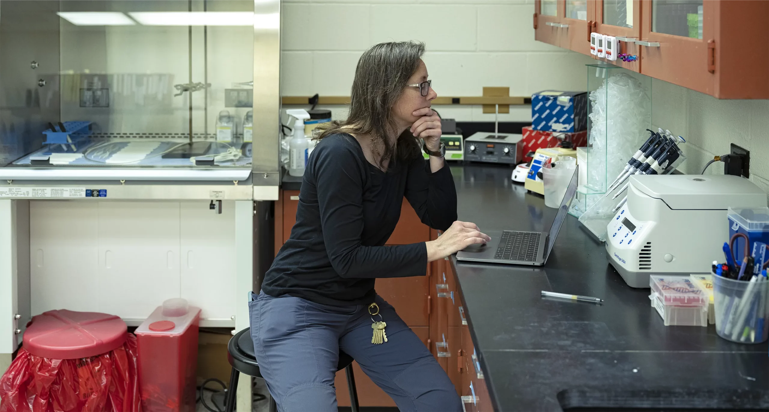 Seimon seated on a stool and working on a laptop on the counter of her laboratory.