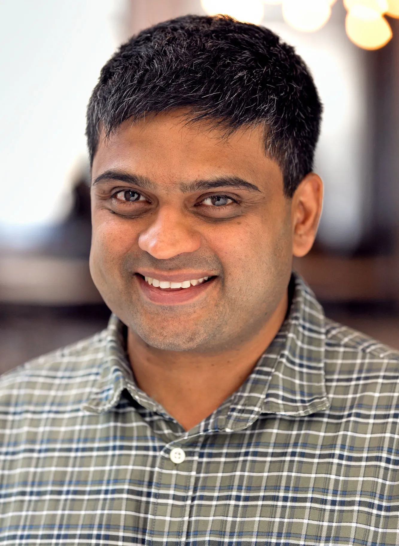 A smiling man wearing a checkered shirt.