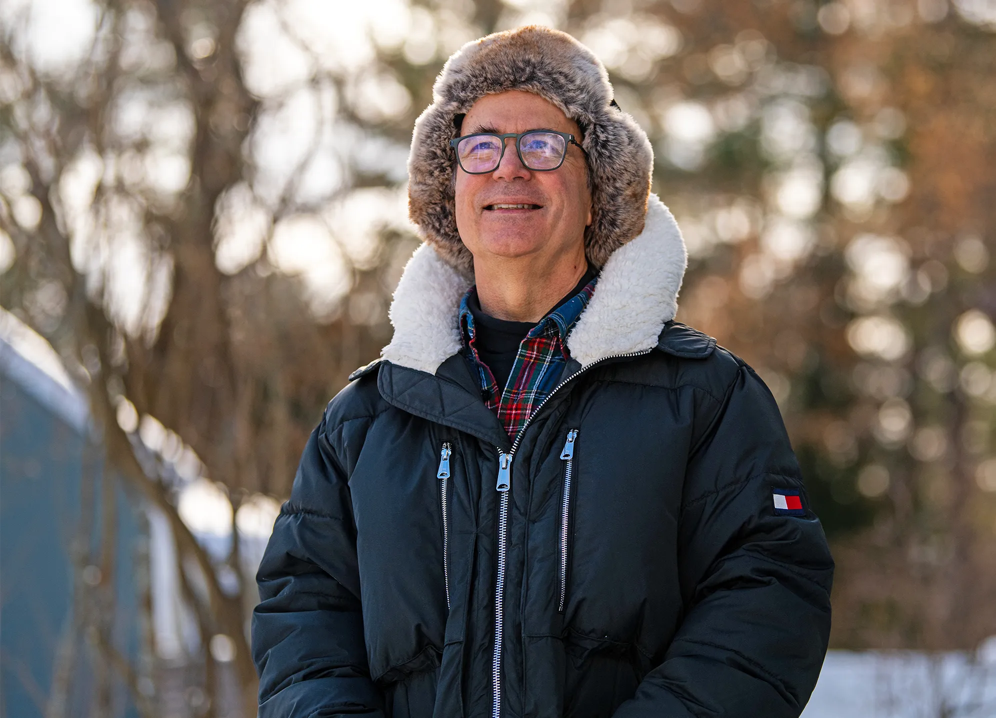 A man wearing eyeglasses, a puffy jacket and a furry hat.