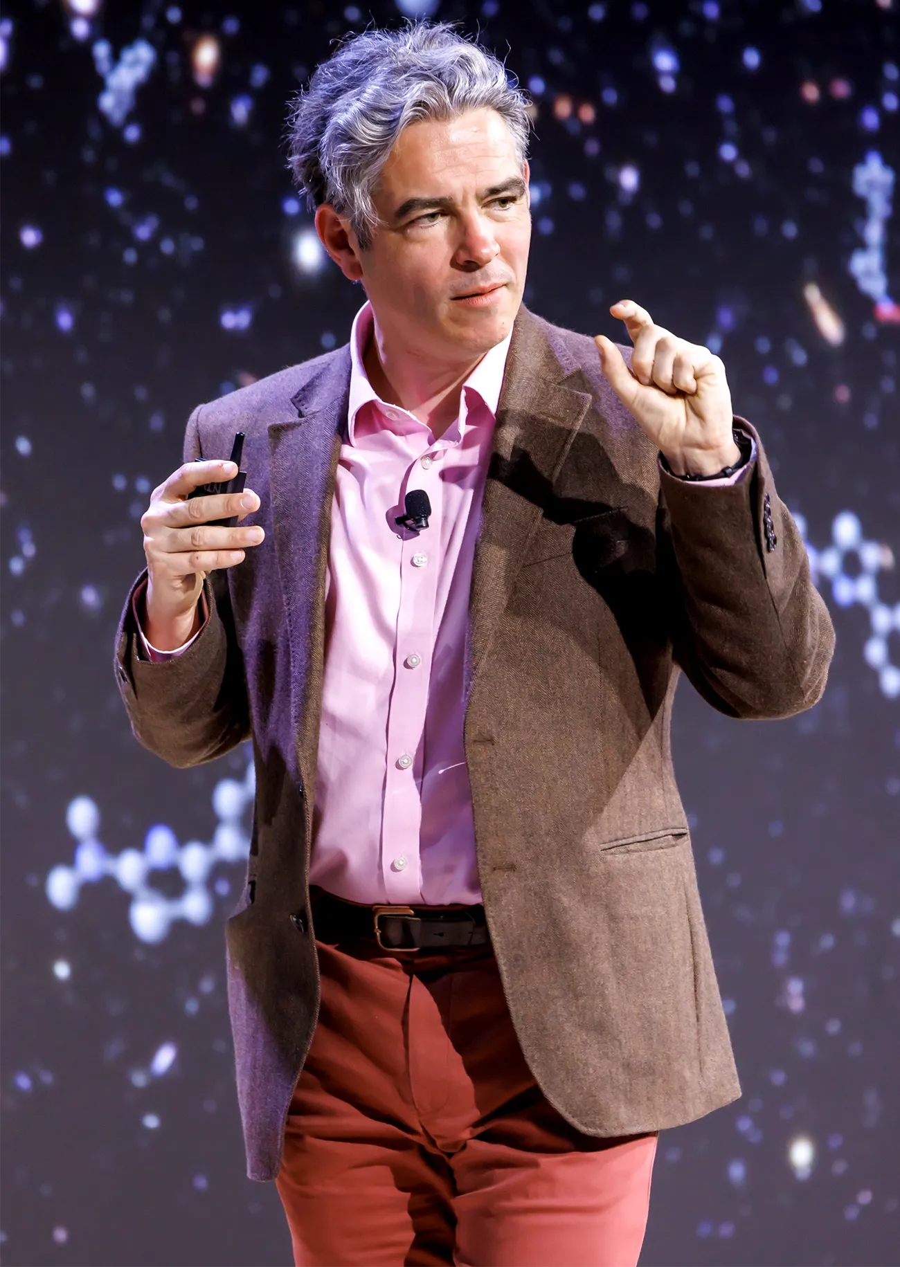 A man in a pink shirt giving a talk on stage.