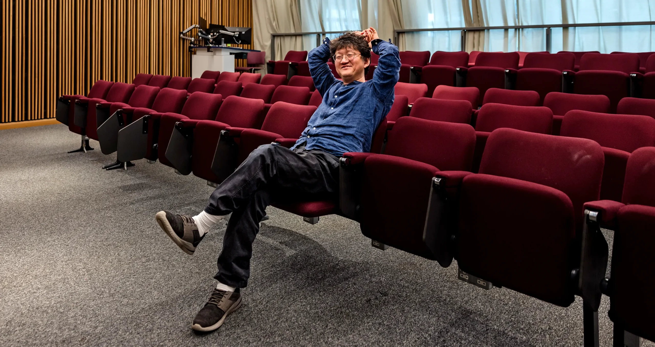 A smiling man sitting on a row of theater seats.