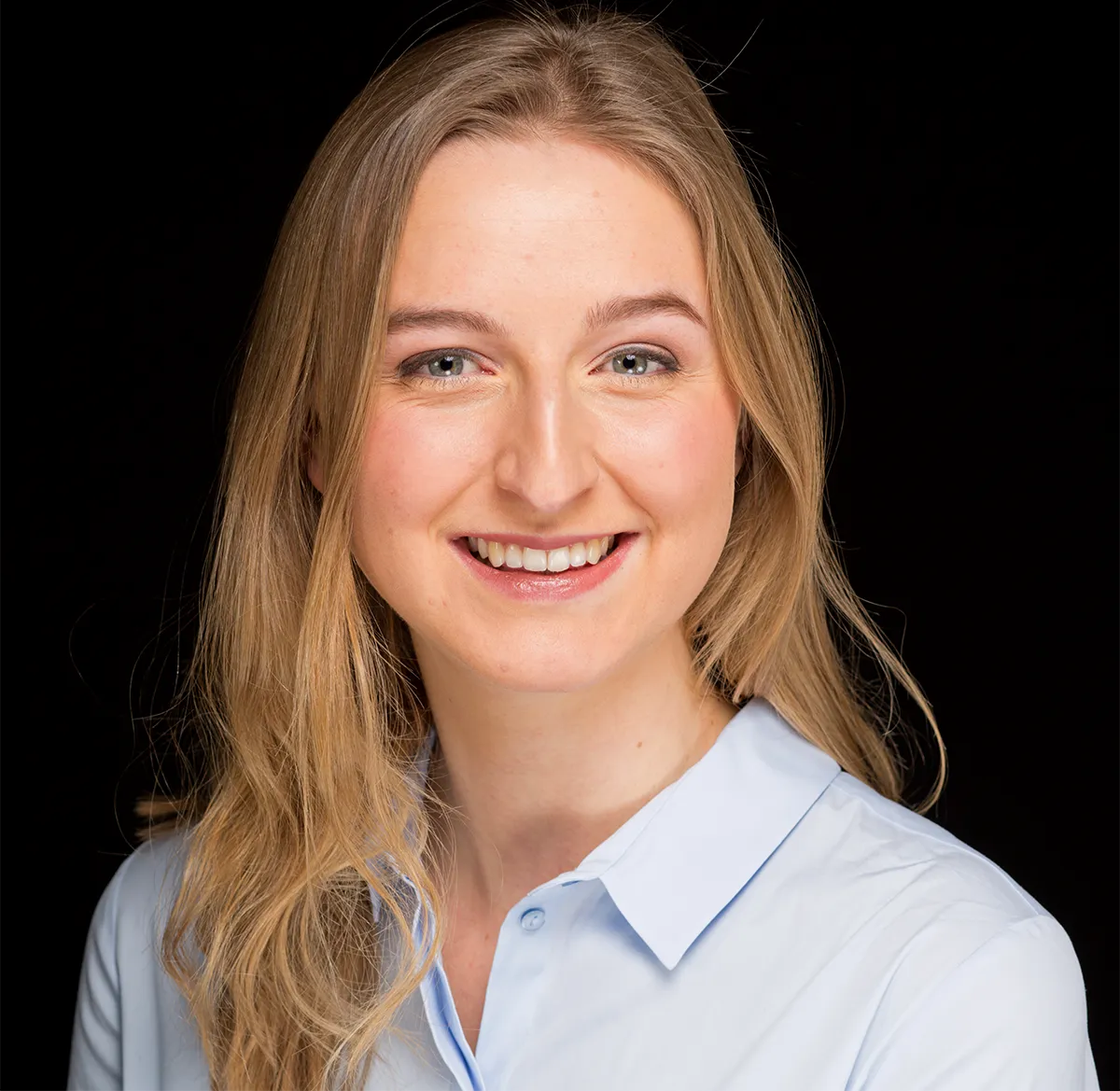 Nora Kassner in a blue shirt against a black background.