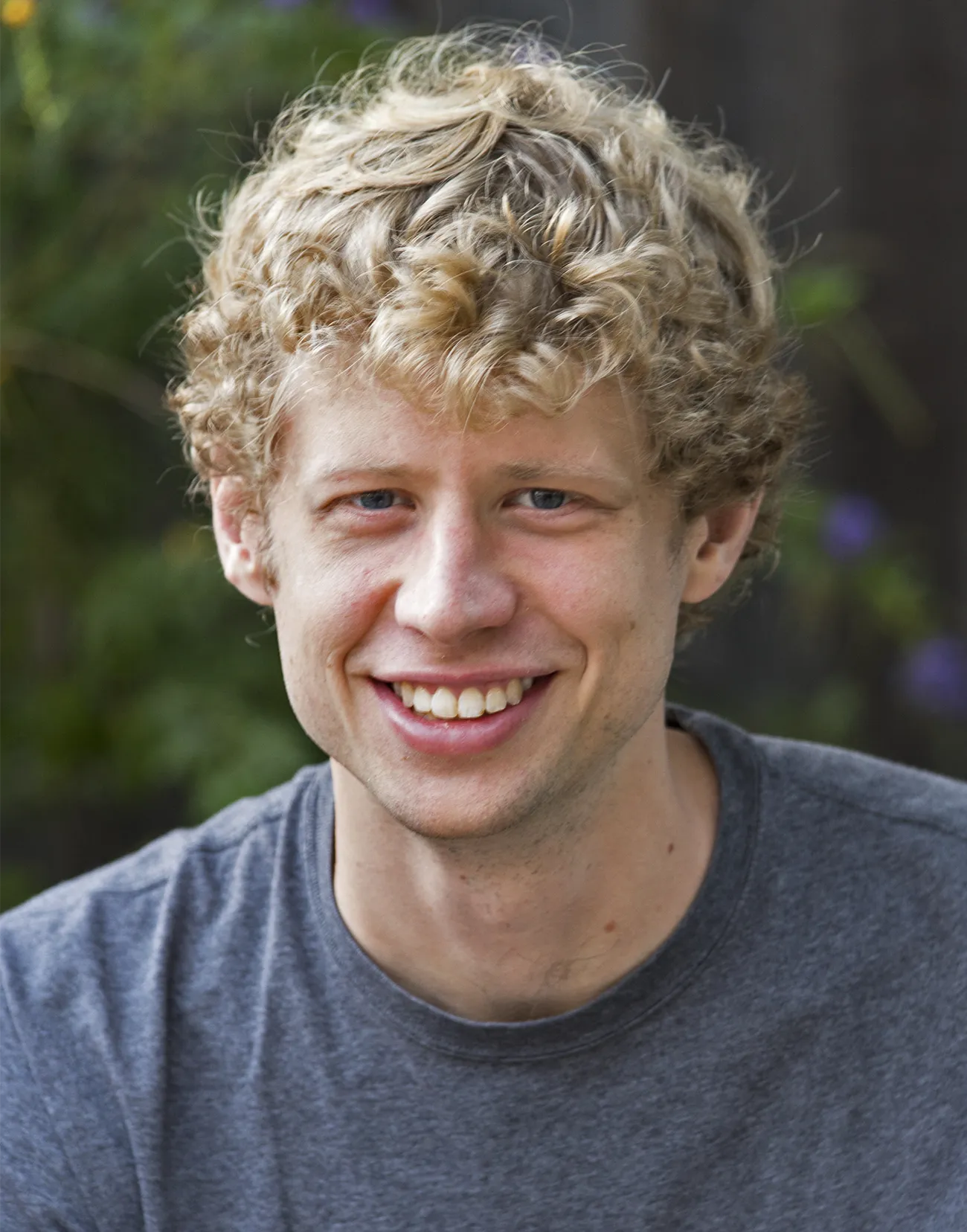 A portrait of Adam Bouland, a smiling man with curly hair.