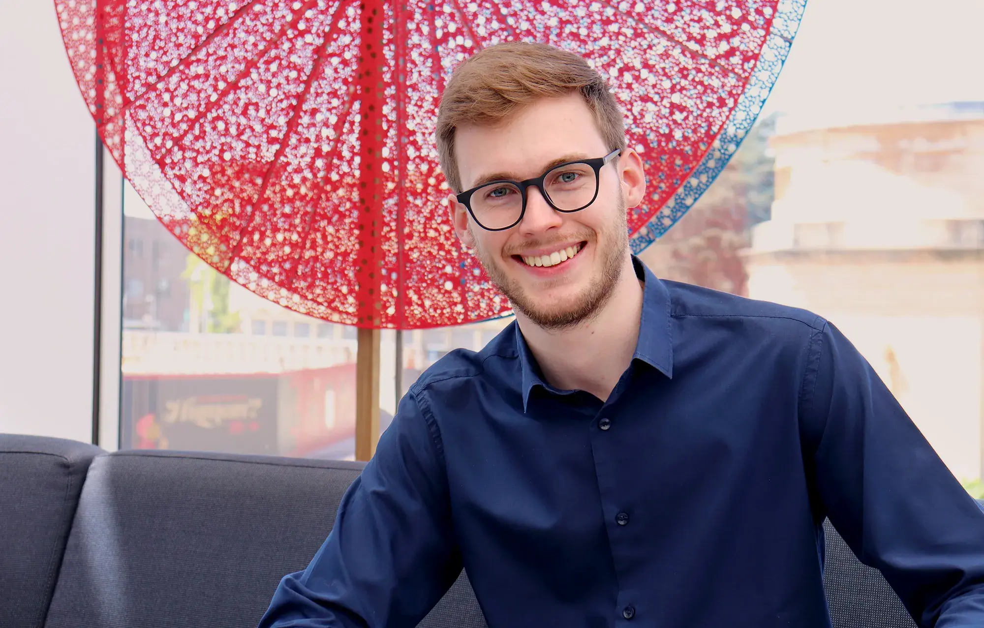 Mathematician Cédric Pilatte smiling wearing a blue shirt and glasses.