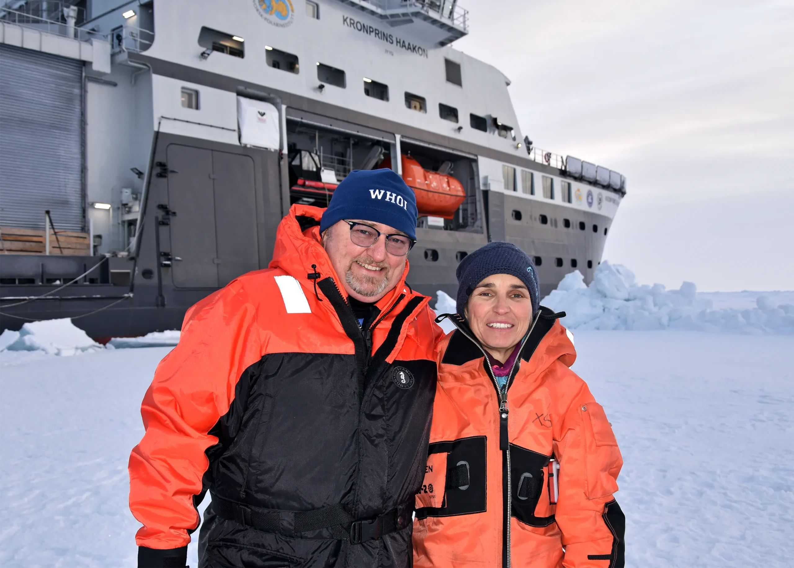 Researchers Chris German and Eva Ramirez-Llodra in parkas on the ice beside an icebreaker ship.