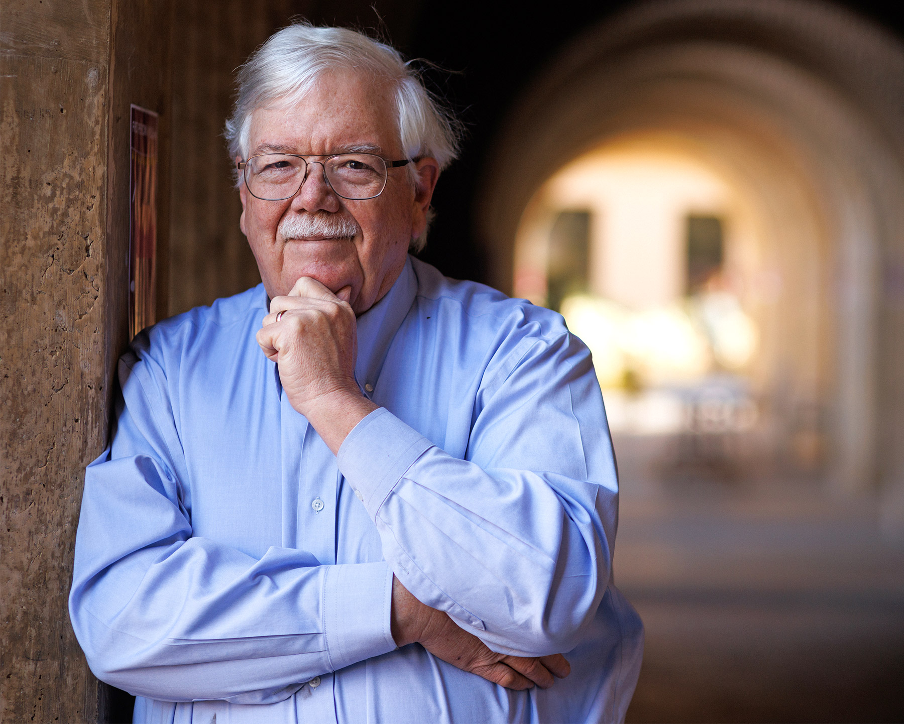 Stanford University law professor Hank Greely leans against a wall in an arched hallway, hand on chin.