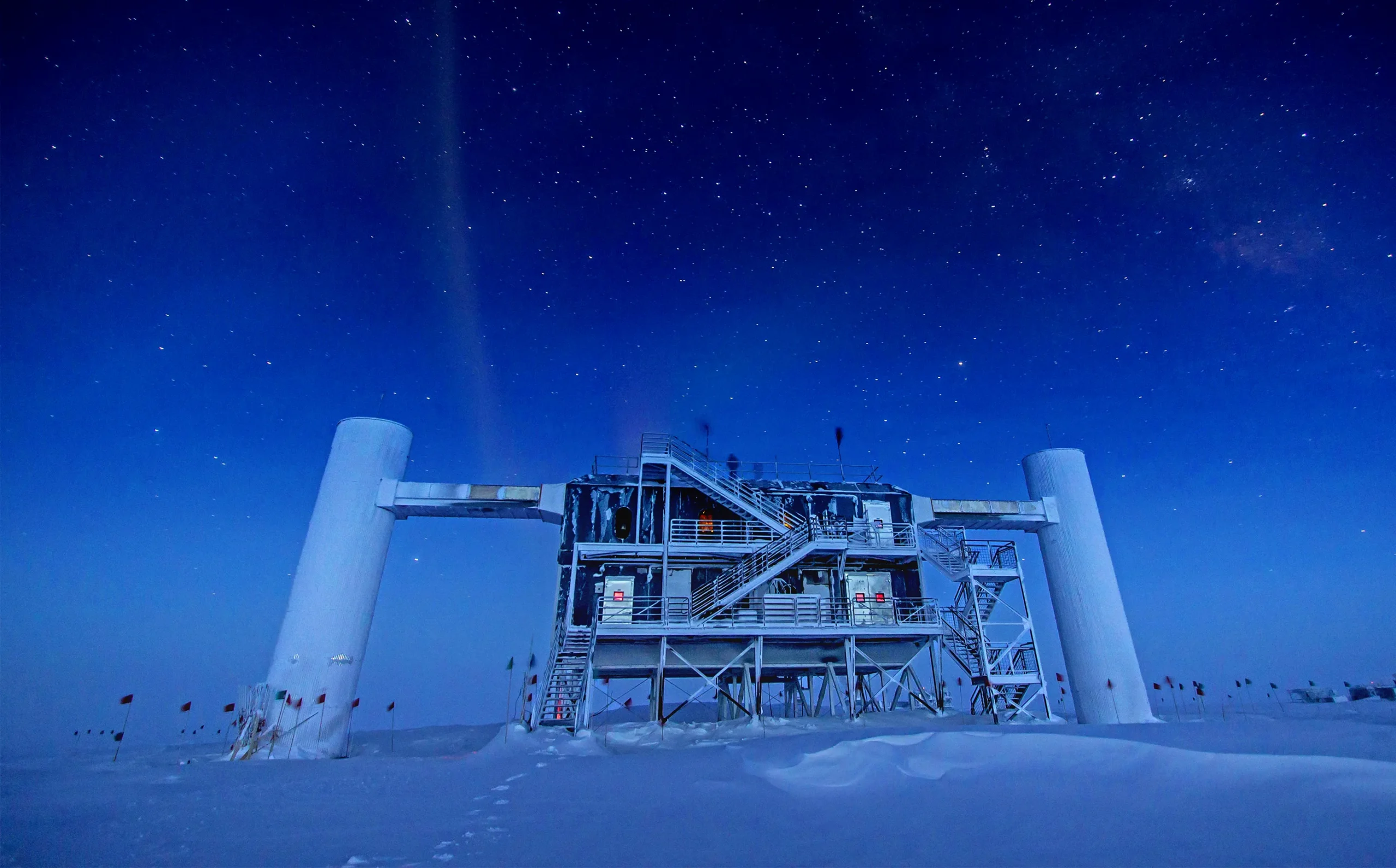 The IceCube Neutrino Observatory on a snowy field with a night sky behind.