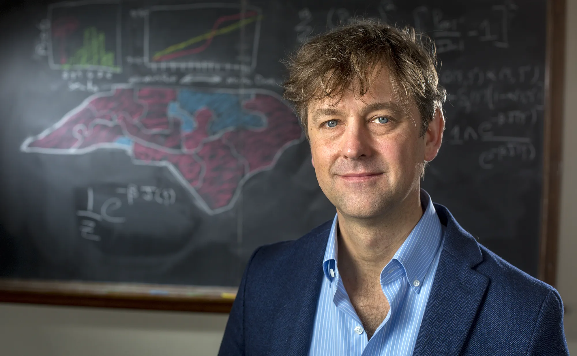 Jonathan Mattingly, a mathematician at Duke University in North Carolina, stands in front of a blackboard with a map of the state drawn on it.