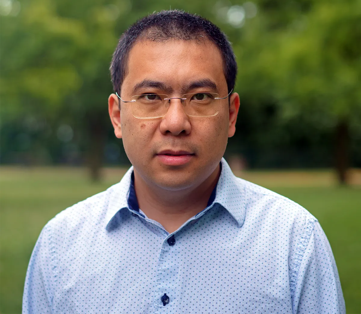 Xiaorui Sun in a blue shirt with trees in the background.