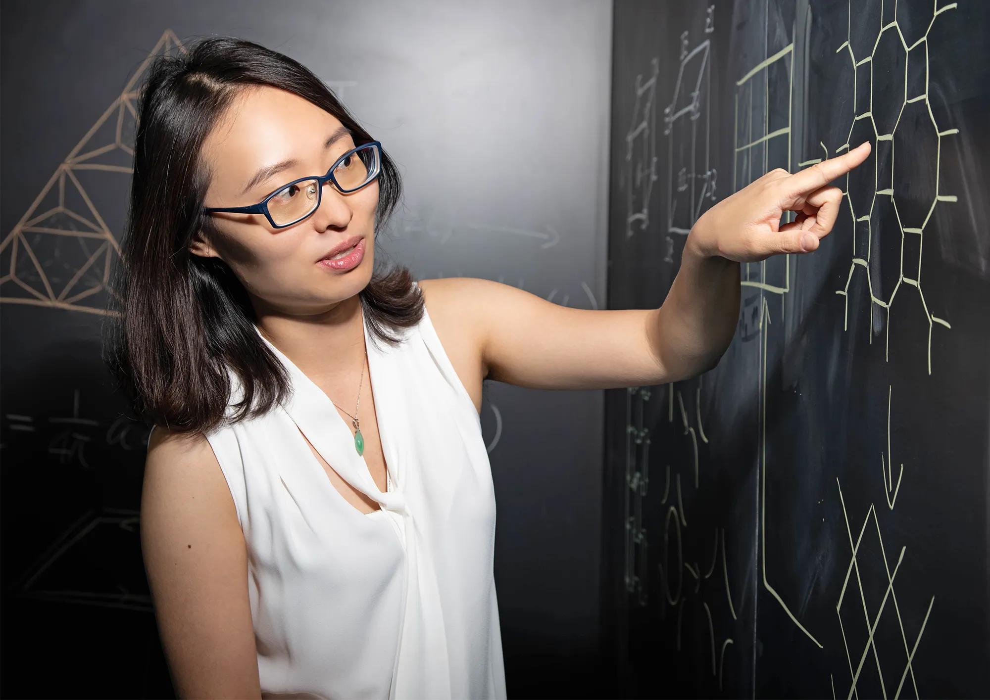 A portrait of Xie Chen pointing at a chalk board.