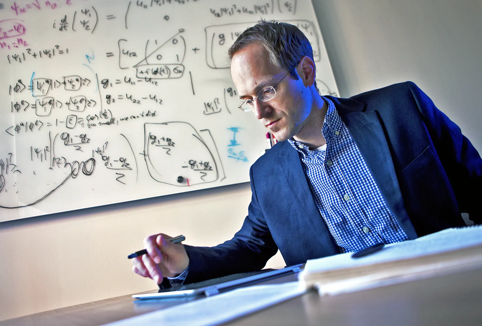 Andrews Childs in a striped shirt and blazer in front of a whiteboard with equations.