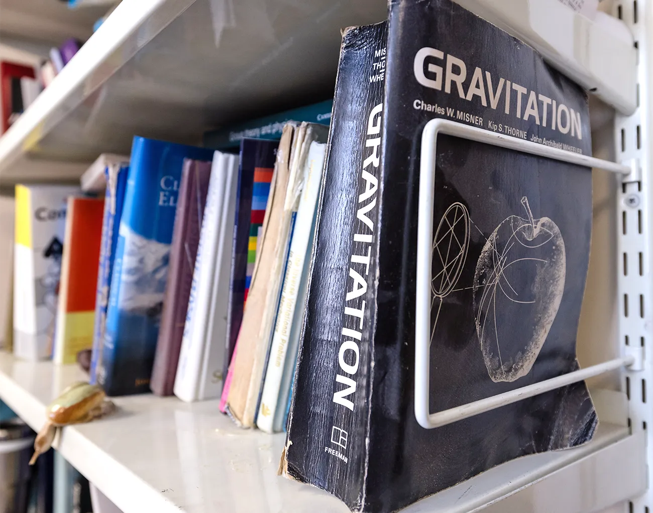 A bookshelf featuring a worn, paperback textbook titled “Gravitation.”