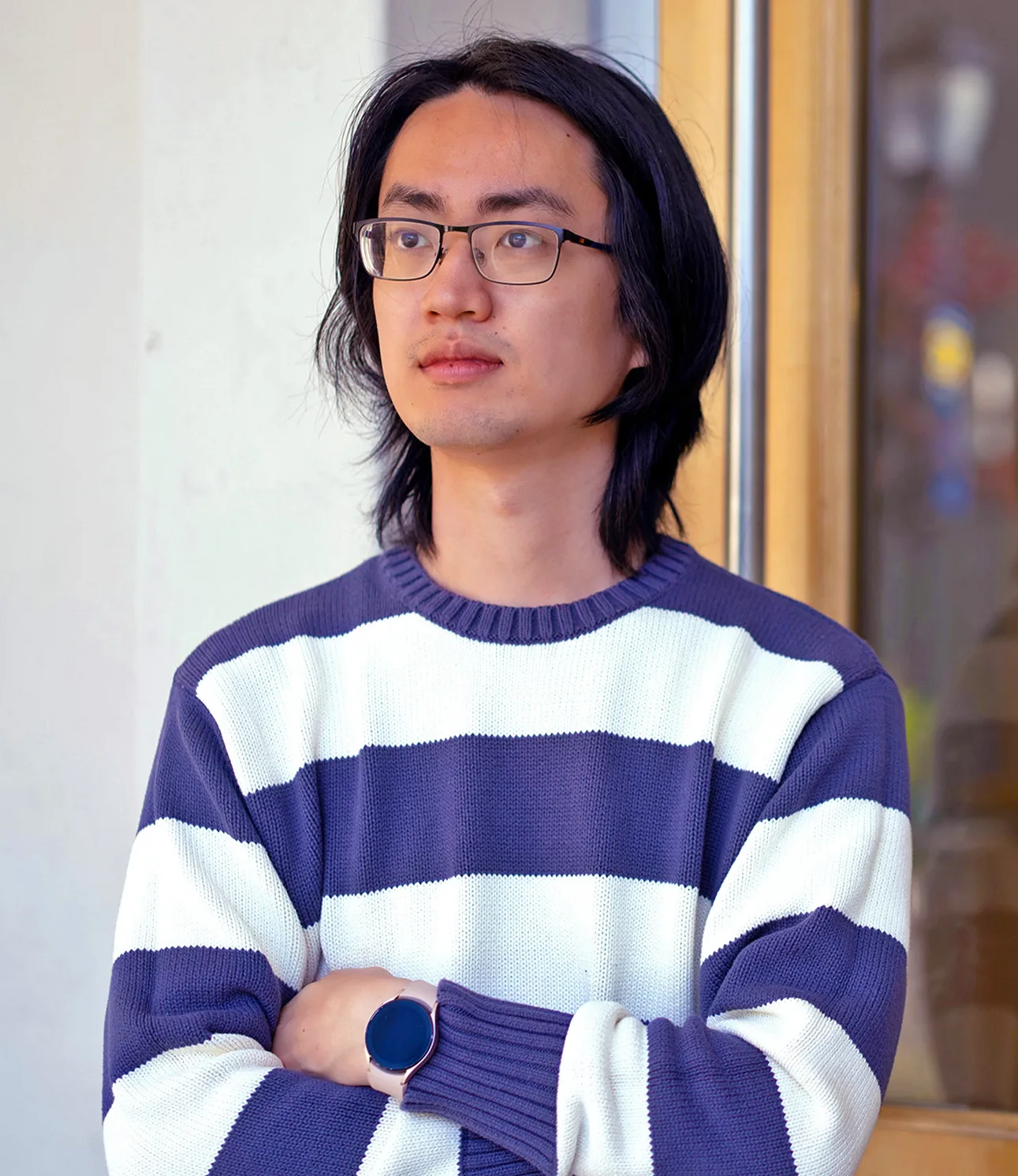 Lijie Chen in a striped sweater stands outside, in front of a door.