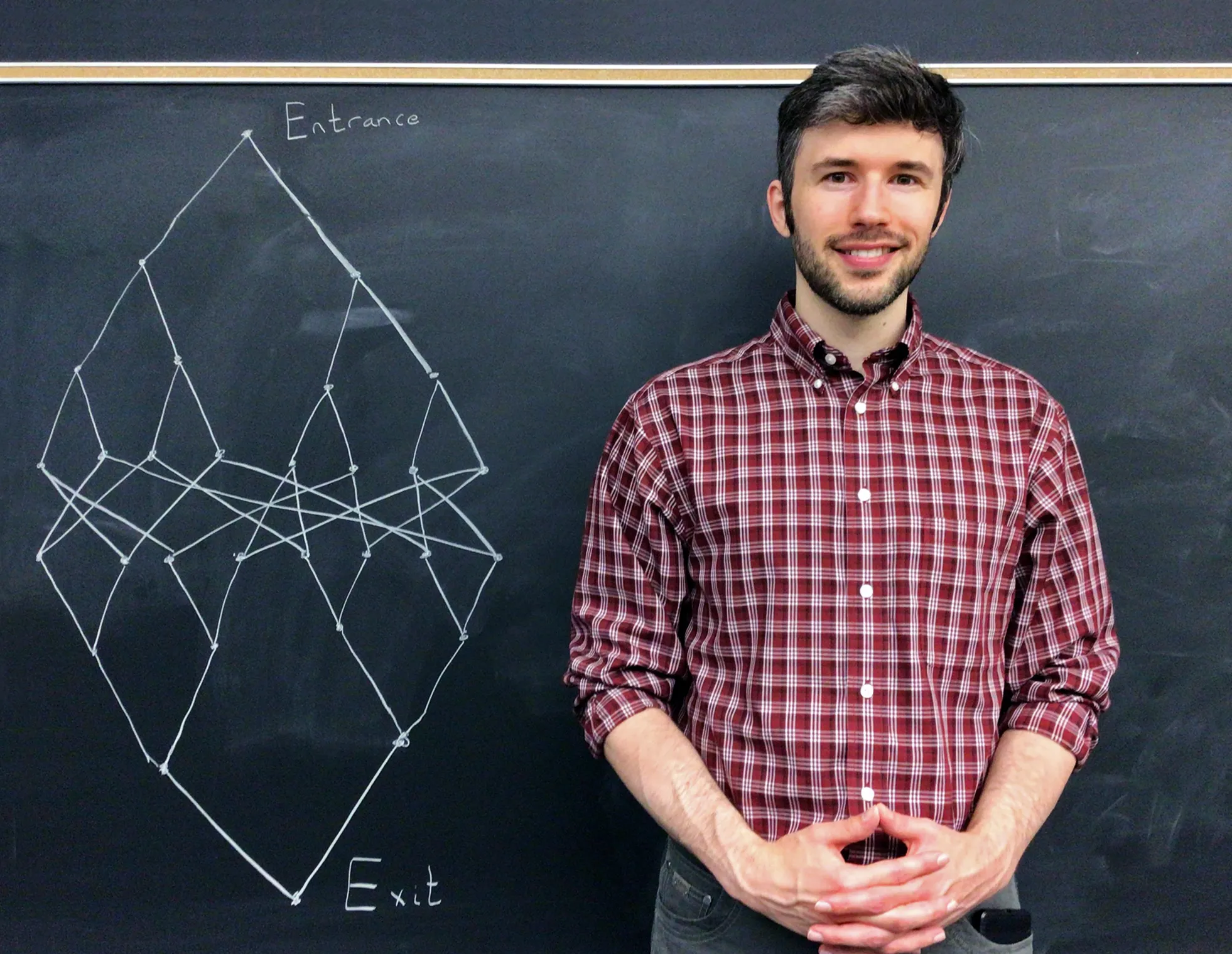 Matthew Coudron in a red checkered shirt in front of a red wall.