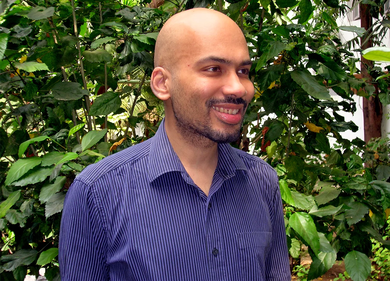 Rahul Santhanam in a striped purple shirt in front of a leafy plant.