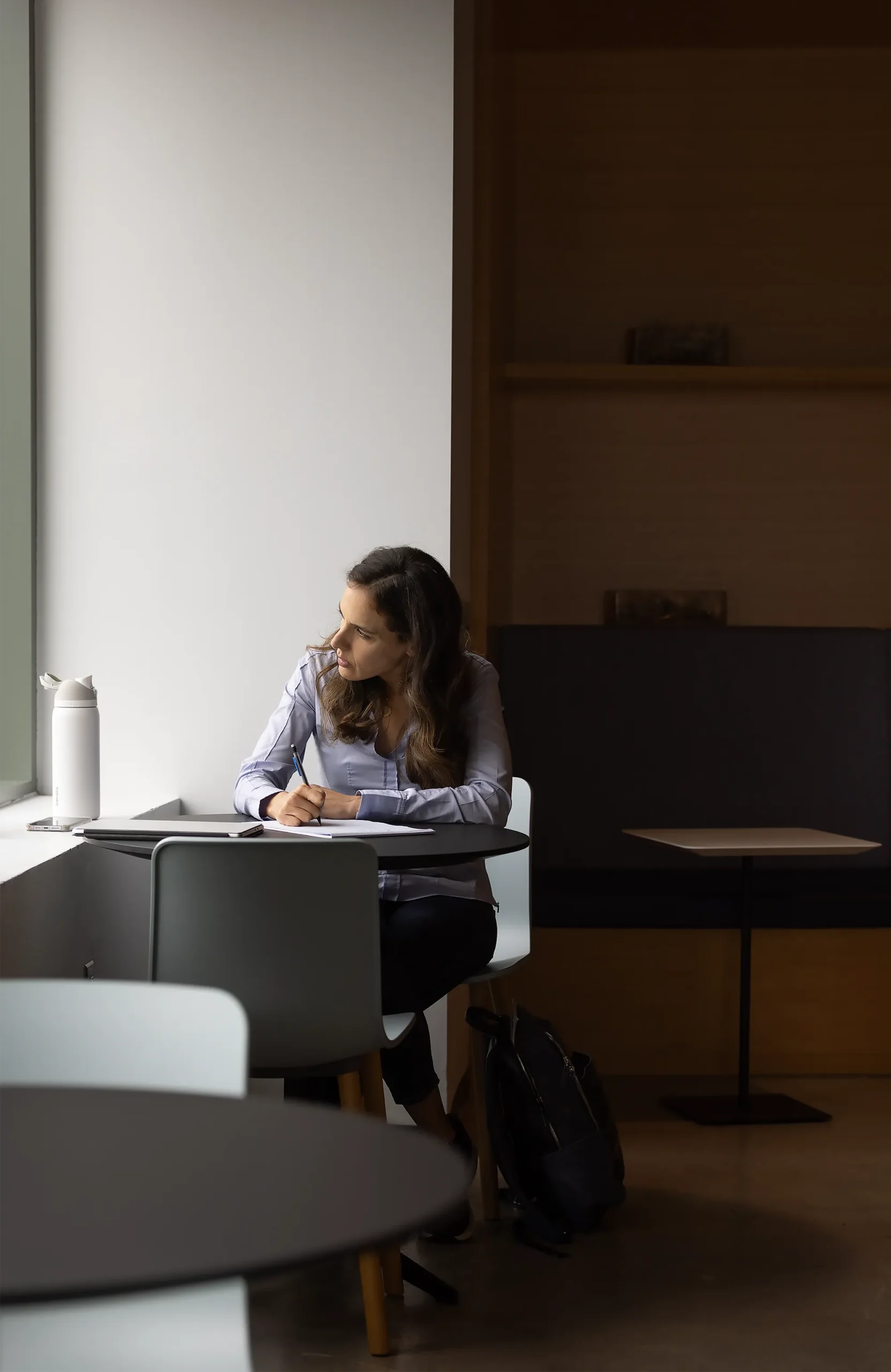 Yael Tauman Kalai, in a blue shirt, sits at a table and looks out a nearby window.