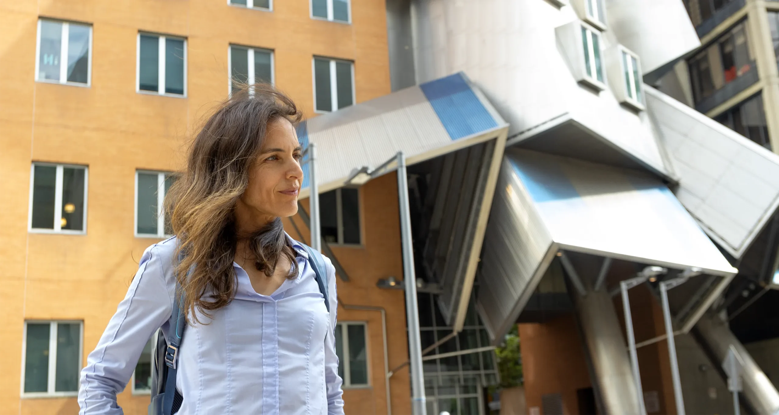 Yael Tauman Kalai, in a blue shirt, stands in front of a crumpled-looking building.