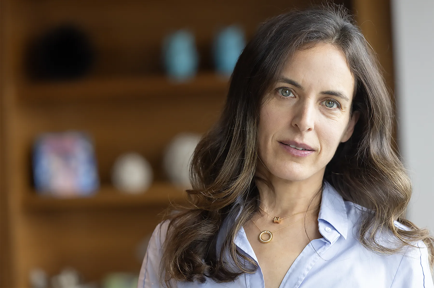 Close-up of Yael Tauman Kalai in a blue shirt, in front of blurry shelves.