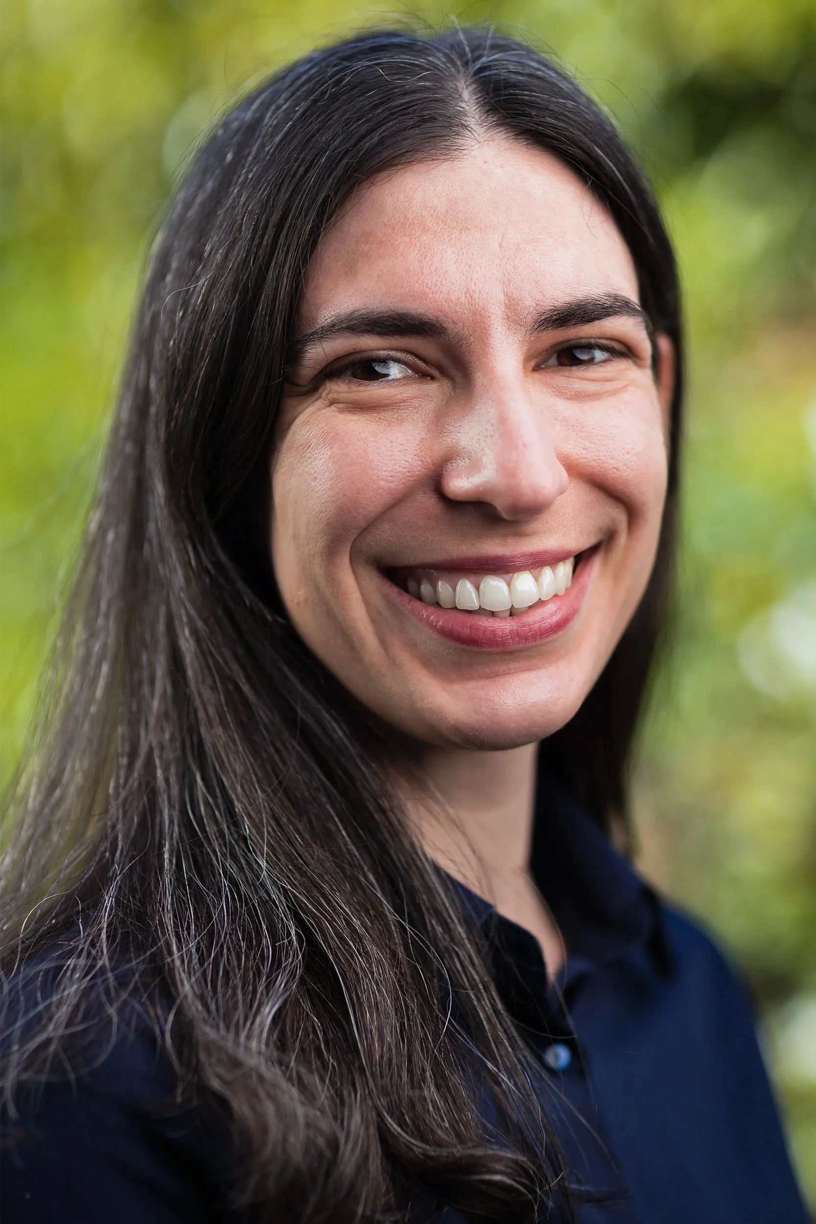 A headshot of Ana Bonaca wearing a black shirt, with trees in the background.