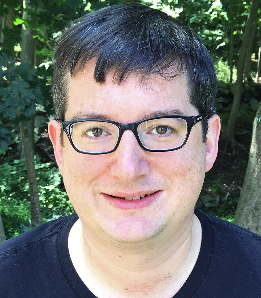 A headshot of Cross, smiling at the camera, with trees in the background.