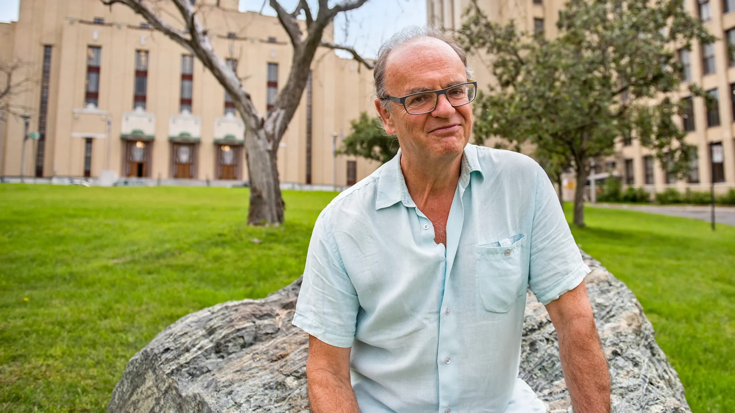 Mathematician Andrew Granville sitting on a rock in a campus quadrangle.