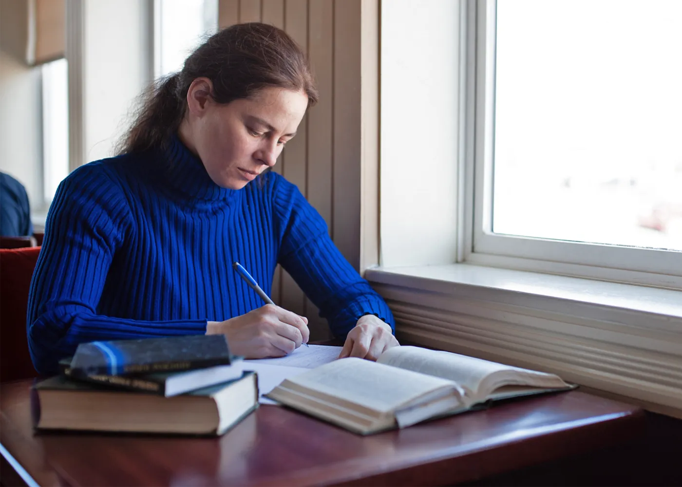 Photograph of Antonina Kolokolova, writing at a desk in a blue sweater.