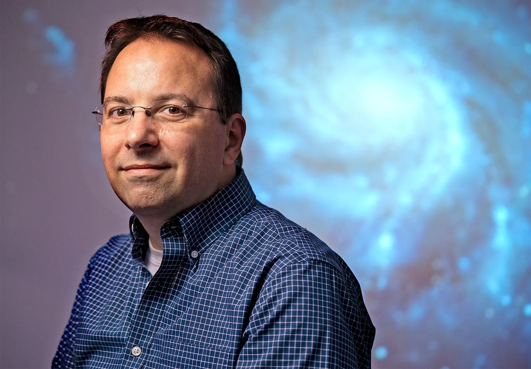 A portrait of Kocevski with a huge spiral galaxy in the background. The galaxy is blurred and Kocevski is in focus.