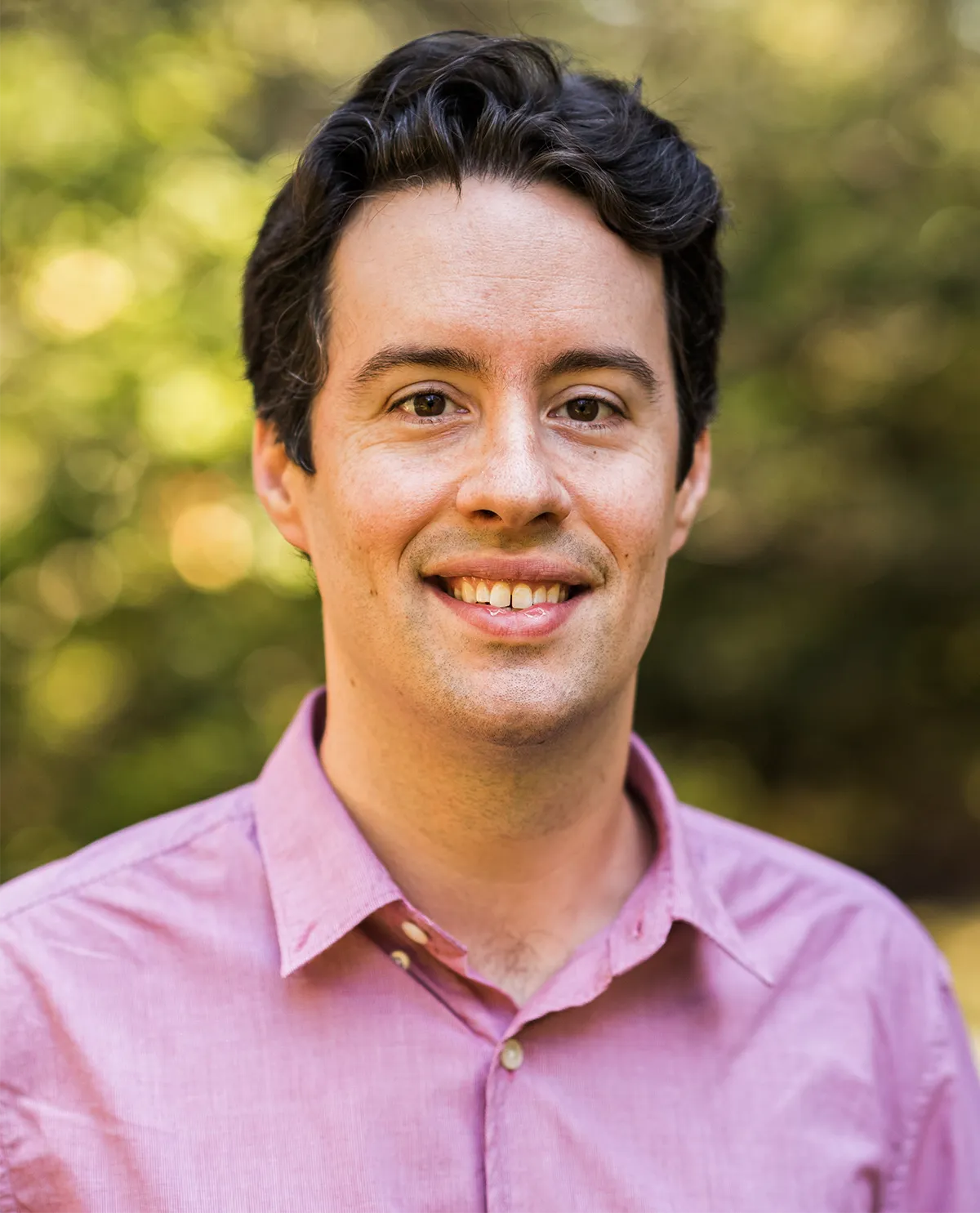 A man in a pink shirt stands outside.