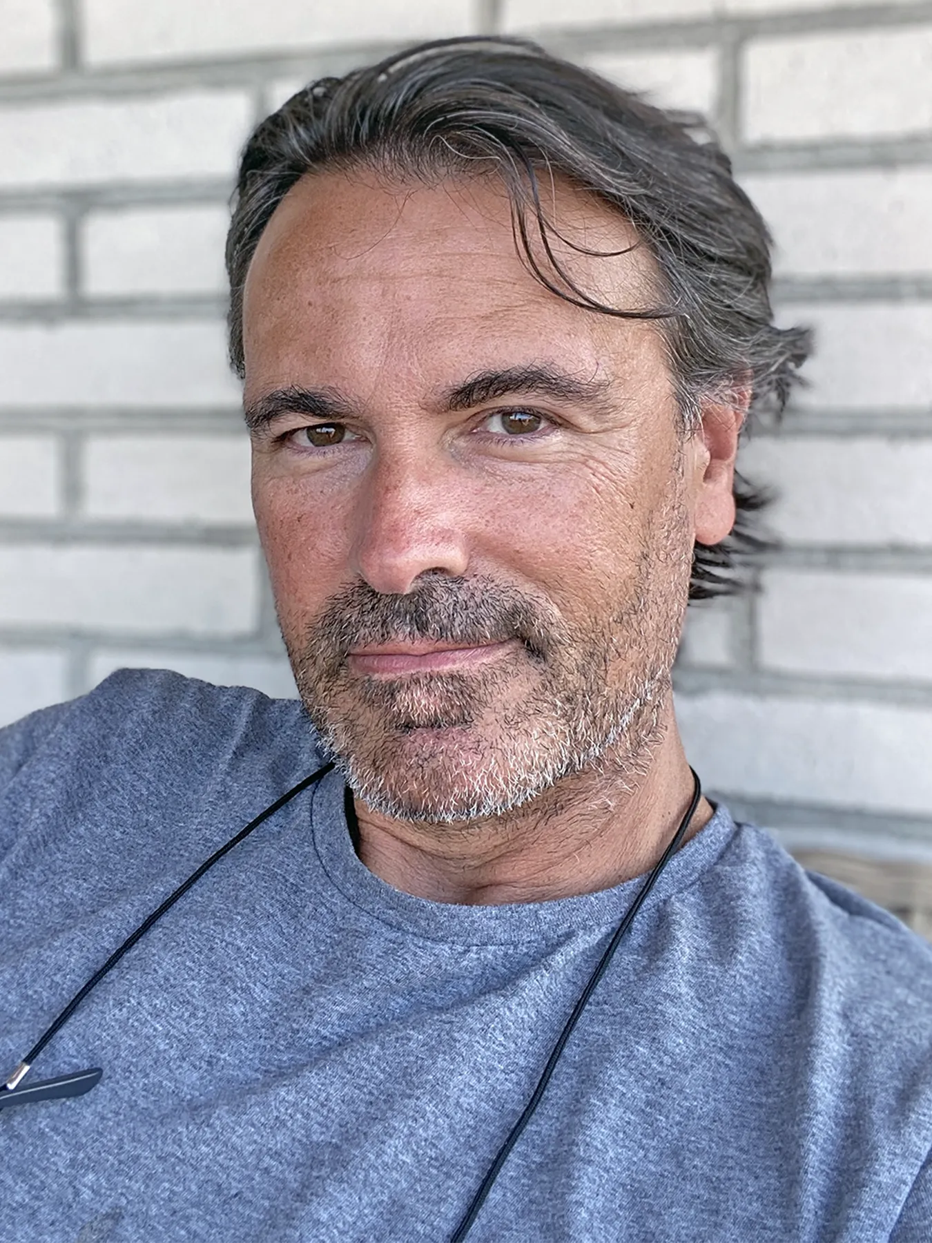 A portrait of José María Diego. He is wearing a blue shirt and is sitting in front of a white-bricked wall.