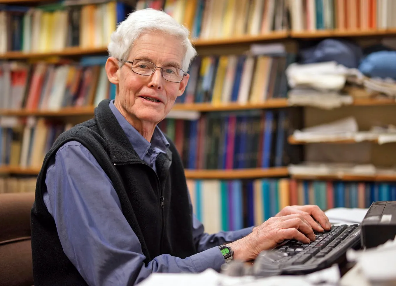 Photograph of Stephen Cook sitting at a desk wearing a fleece vest.