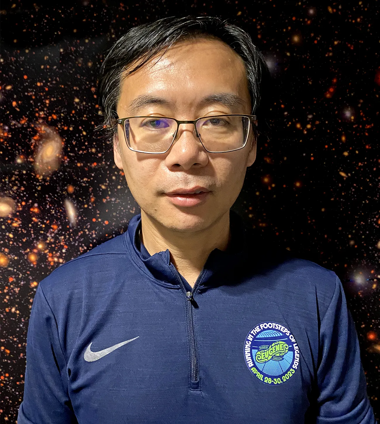 Fan is standing in front of an astronomical backdrop in which swirling galaxies are surrounded by sparkling stars.